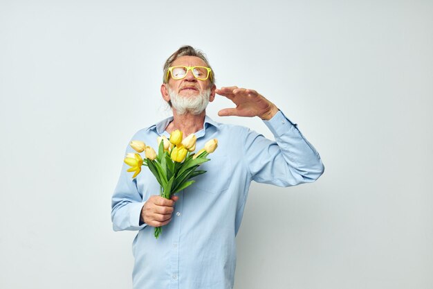 Retrato de homem sênior feliz em uma camisa azul com um buquê de flores de fundo claro