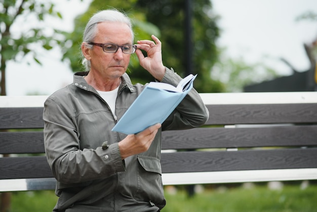 Retrato de homem sênior lendo no banco durante o dia de verão