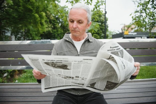 Retrato de homem sênior lendo no banco durante o dia de verão