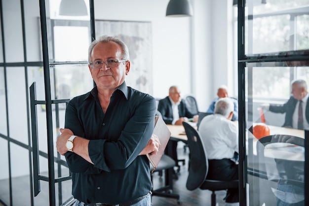 Retrato de homem sênior que fica na frente da equipe envelhecida de arquitetos idosos empresário que têm uma reunião no escritório.