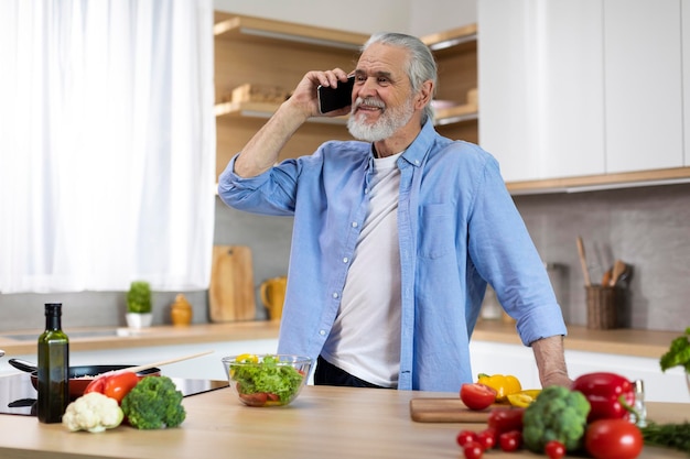 Retrato de homem sênior sorridente falando no celular no interior da cozinha