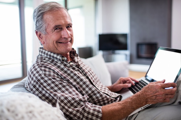 Retrato de homem sênior usando laptop na sala de estar