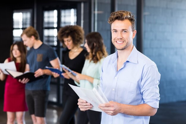 Retrato, de, homem sorridente, segurando, um, documento, enquanto, dela, colegas, estar, dela, em, escritório