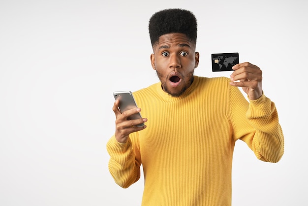 Retrato de homem surpreso casual segurando cartão bancário e telefone isolado no fundo branco