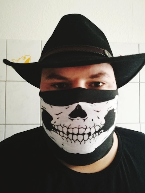 Foto retrato de homem usando máscara de crânio e chapéu contra a parede