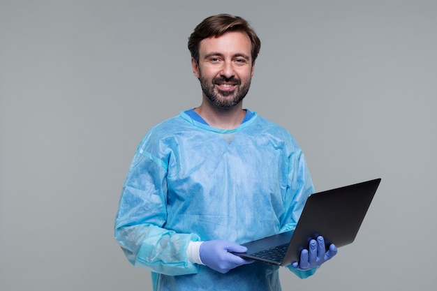 Retrato de homem vestindo bata médica e segurando laptop