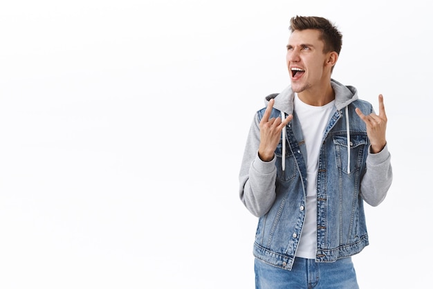 Retrato de homem vibrando no show incrível Cara bonito loiro olhando para a esquerda e mostra o gesto rockon gritando cantando músicas no festival curtindo a festa em pé fundo branco