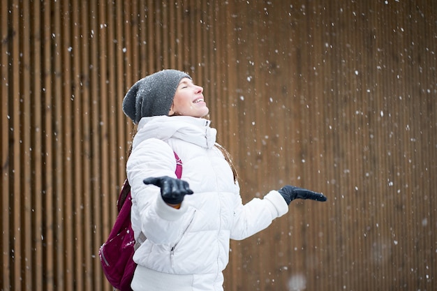 Retrato de inverno ao ar livre. Feliz fofa sorridente caucasiana garota vestida com jaqueta branca, apreciando a primeira neve com os olhos fechados.