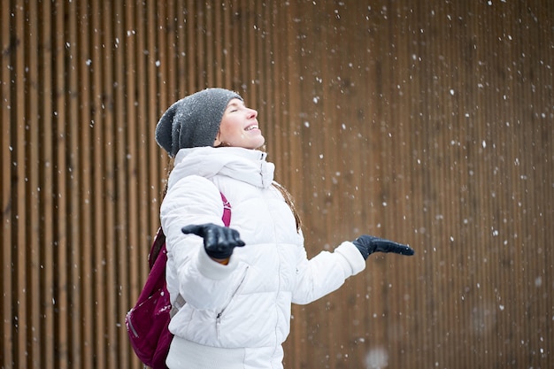 Retrato de inverno ao ar livre. feliz fofa sorridente caucasiana garota vestida com jaqueta branca, apreciando a primeira neve com os olhos fechados.