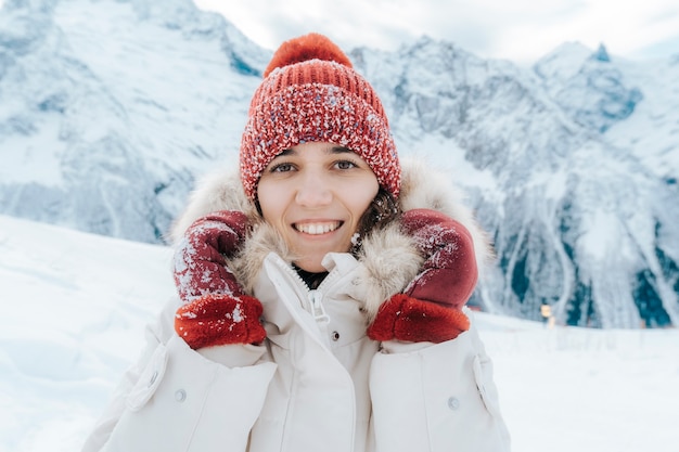 Retrato de inverno de uma jovem em uma jaqueta branca, chapéu e luvas, contra o pano de fundo de montanhas. a garota na neve.