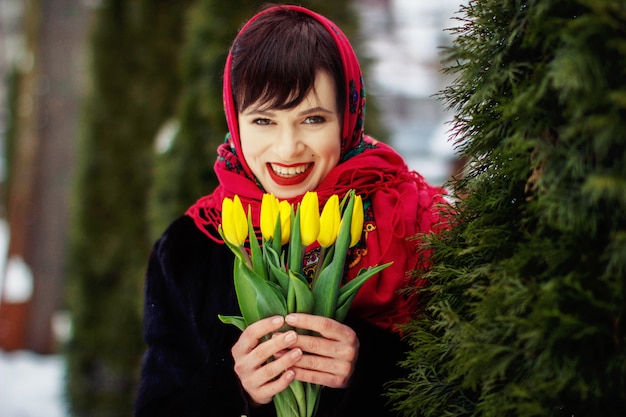 Retrato de Inverno de uma jovem garota em um lenço vermelho. segurando tulipas