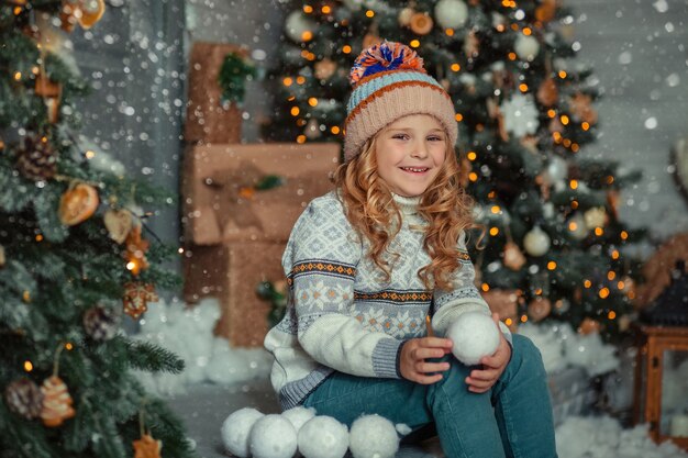 retrato de inverno na varanda perto da casa de uma menina com um chapéu e um suéter