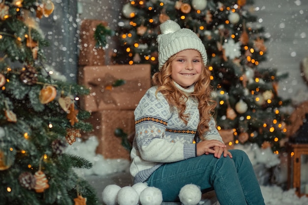 retrato de inverno na varanda perto da casa de uma menina com um chapéu e um suéter