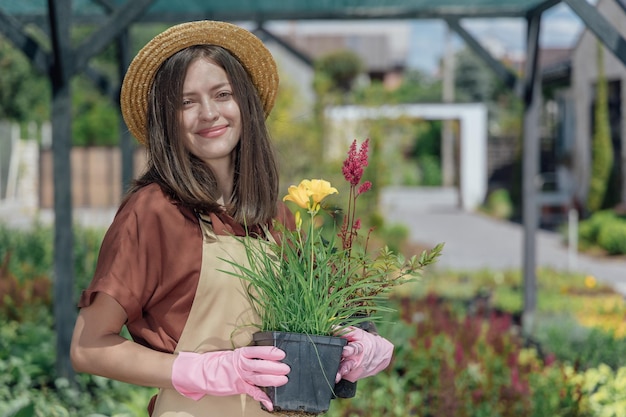 Retrato de jardineira segurando uma planta perene nas mãos e trabalhando perto da casa do jardim