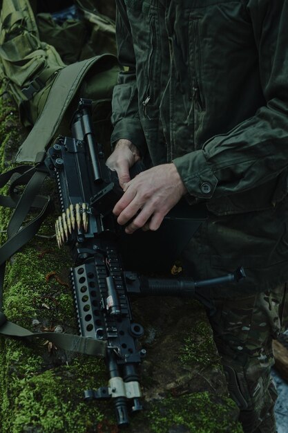 Retrato de jogador de airsoft em equipamento profissional carrega uma arma com balas na floresta. Soldado com armas em guerra