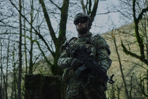 Retrato de jogador de airsoft em equipamento profissional com metralhadora na floresta. soldado com armas em guerra