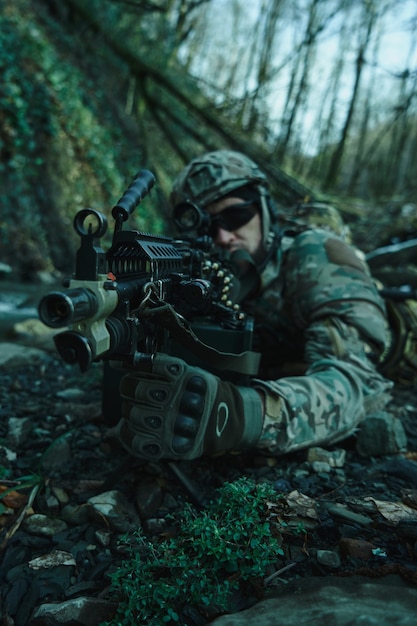 Retrato de jogador de airsoft em equipamento profissional em capacete visando a vítima com arma na floresta. soldado com armas em guerra