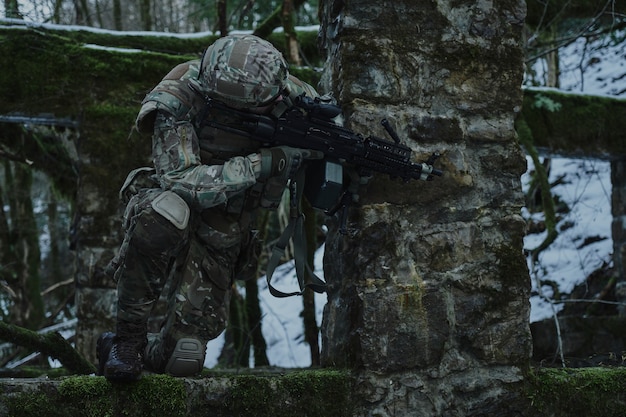 Retrato de jogador de airsoft em equipamento profissional em capacete visando a vítima com arma na floresta. Soldado com armas em guerra