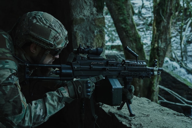 Foto retrato de jogador de airsoft em equipamento profissional em capacete visando a vítima com arma na floresta. soldado com armas em guerra