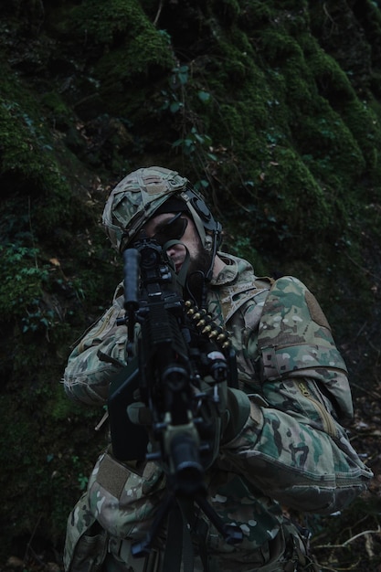 Retrato de jogador de airsoft em equipamento profissional em capacete, visando a vítima com arma na floresta. Soldado com armas em guerra