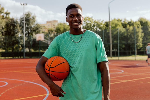 Retrato de jogador de basquete americano africano encantado em pé na quadra de basquete com bola