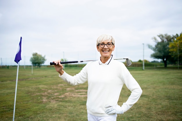 Retrato de jogador de golfe feminino sênior com clube de golfe em pé no campo de golfe.