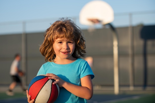 Retrato de jogo infantil de basquete de menino bonitinho segurando uma bola de basquete tentando fazer uma pontuação