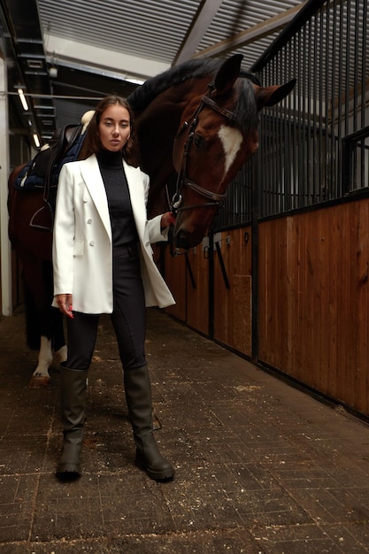 Retrato de jóquei feminino sorridente em pé a cavalo no estábulo