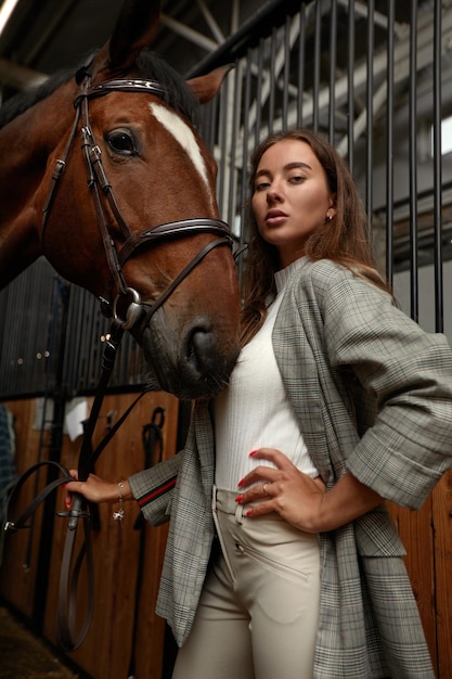 Retrato de jóquei feminino sorridente em pé a cavalo no estábulo