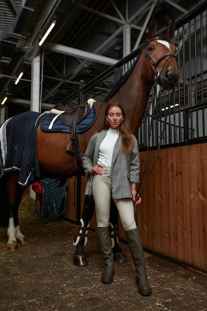 Retrato de jóquei feminino sorridente em pé a cavalo no estábulo