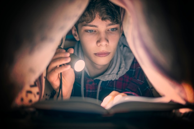 Retrato de jovem adolescente lendo um livro com uma luz debaixo do cobertor à noite f