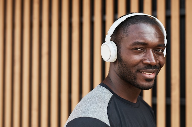 Retrato de jovem africano em fones de ouvido sem fio, sorrindo para a câmera enquanto caminha pela cidade