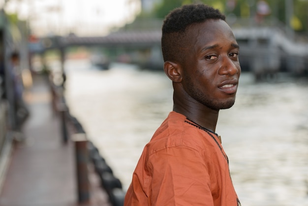 Retrato de jovem africano vestindo roupas tradicionais contra a vista do rio ao ar livre da cidade