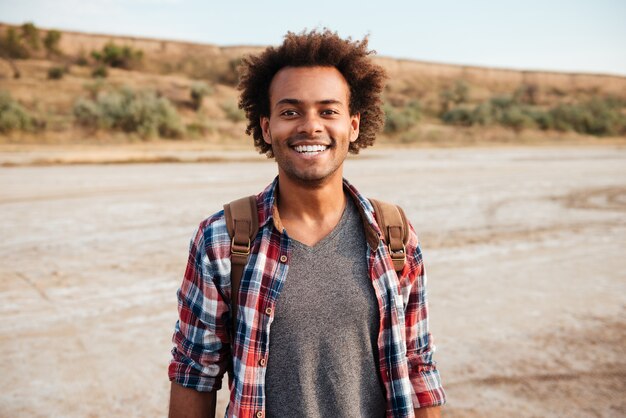 Retrato de jovem afro-americano alegre em camisa xadrez com mochila