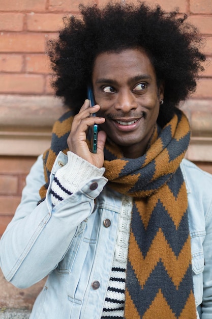 Retrato de jovem afro-americano com penteado afro e roupas da moda falando ao telefone ao ar livre.