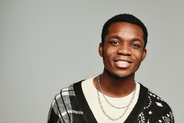 Retrato de jovem afro-americano sorrindo para a câmera contra um fundo cinza.