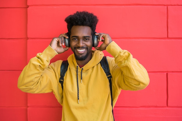 Retrato de jovem afro ouvindo música com fones de ouvido contra o espaço vermelho. Conceito de tecnologia.
