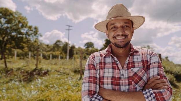 Foto retrato de jovem agricultor com mãos cruzadas na camisa casual e chapéu na fazenda