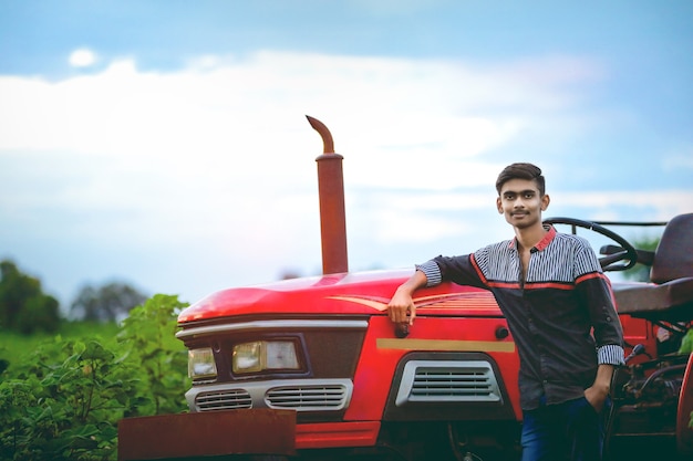 Retrato de jovem agricultor indiano em campo com trator