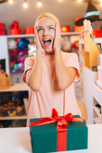 Retrato de jovem alegre animado em pé perto da mesa com caixa de presente de Natal embrulhada ...