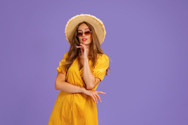 Retrato de jovem animado em óculos de sol de chapéu de verão vestido amarelo posando isolado em viol pastel.