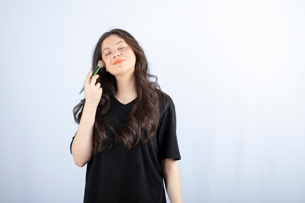 Retrato de jovem aplicando blush nas bochechas em branco.