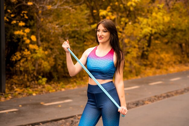 Retrato de jovem apto com corda de pular no parque outono. Fêmea de aptidão segurando a corda de pular antes de seu treino ao ar livre. Ela usa roupas esportivas brilhantes. Garota esportiva está sorrindo