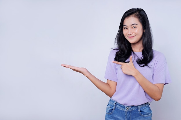 Retrato de jovem asiática sorrindo com uma expressão alegre, mostra algo incrível no espaço em branco em um pano casual isolado com parede