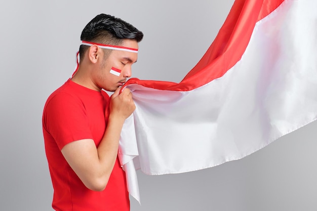 Retrato de jovem asiático beijando a bandeira indonésia isolada em fundo branco conceito de dia da independência indonésia