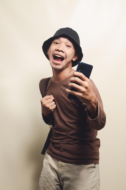 Retrato de jovem asiático com expressão de luta usando chapéu preto e carregando mochila