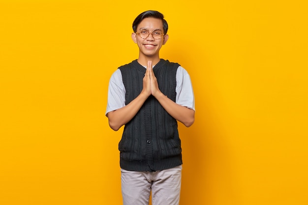 Retrato de jovem asiático feliz segurando a mão sobre fundo amarelo