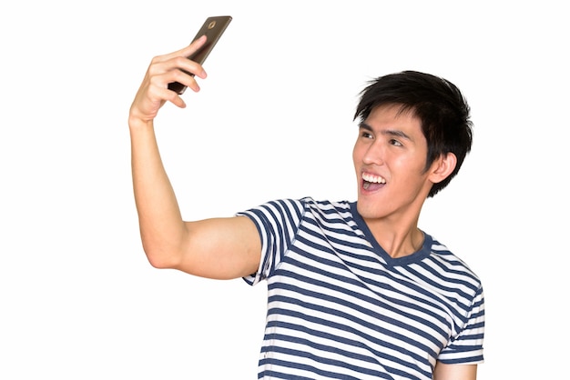 Retrato de jovem asiático feliz tirando selfie com o celular isolado contra uma parede branca