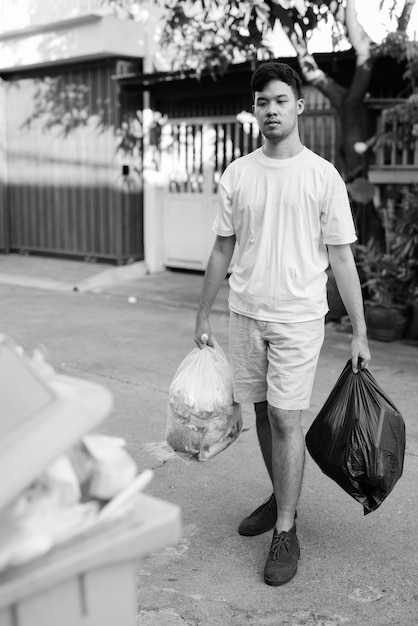 Retrato de jovem asiático levando o lixo para fora de casa