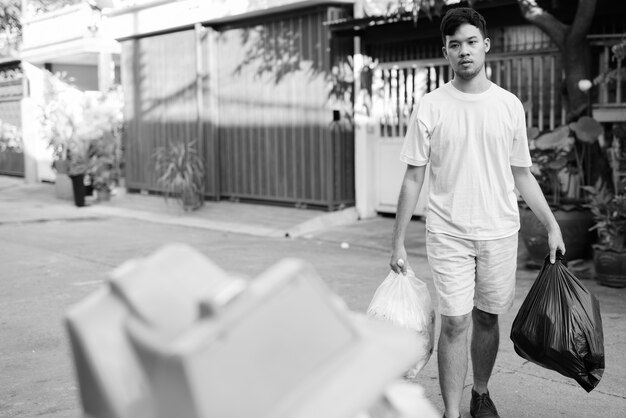 Retrato de jovem asiático levando o lixo para fora de casa